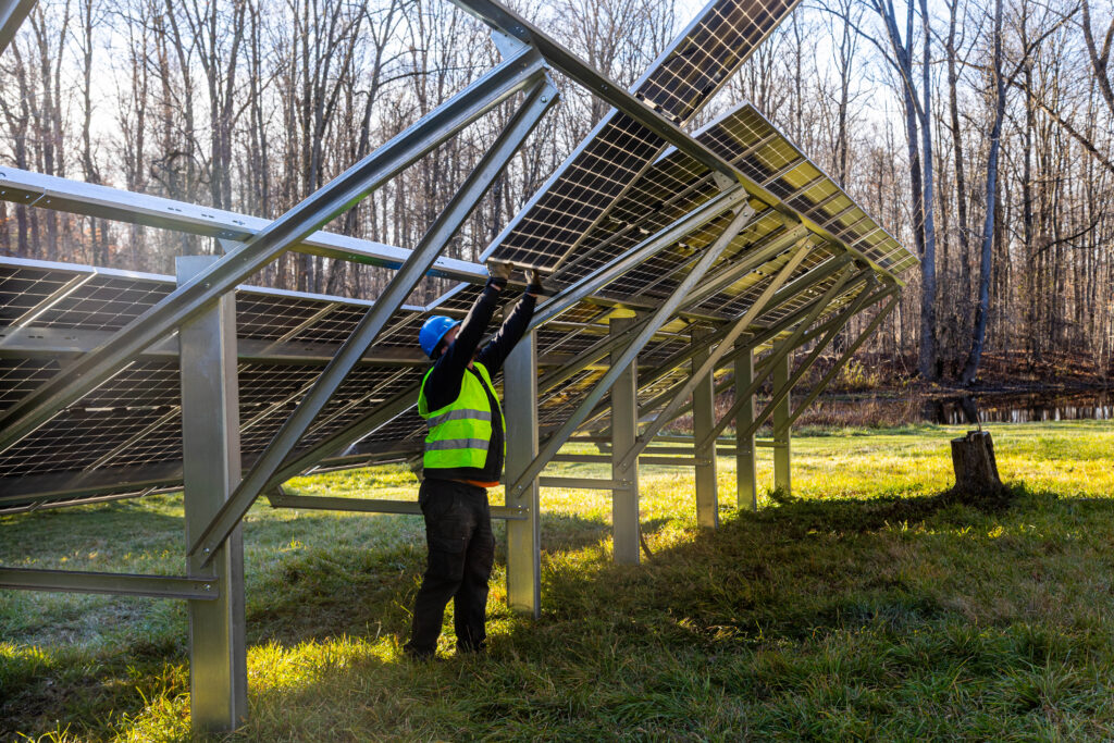 solar installer in a neon vest and hardhat installing a solar panel onto a solar array